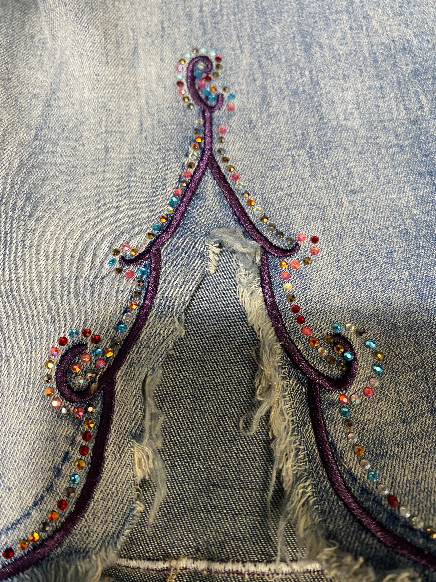Close-up of a decorative cut sleeve design on denim jacket with colorful beads and intricate patterns.